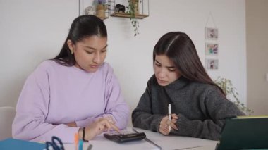 Akademik ödevde birlikte çalışan bayan üniversite öğrencileri, evde öğrenim alanında bilgi paylaşırken ayrıntıları hesaplıyor ve not alıyorlar