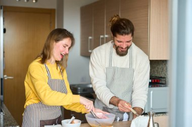 Neşeli çift kahvaltı hazırlarken ya da mutfaklarında kek pişirirken yumurta çırpıyor ve gülüyor.