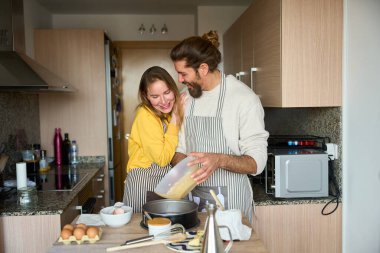 Önlük takan bir çift kek hamurunu pişirme tavasına döküyor, birlikte vakit geçiriyorlar, parlak, modern bir mutfakta.