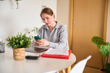 Evde çalışan serbest çalışan, akıllı telefon ve dizüstü bilgisayar kullanan, rahat çalışma ortamında iş ve finansman yöneten