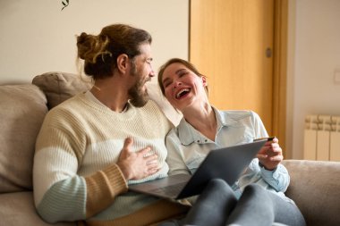 Mutlu çift online alışverişler yaparken bir yandan da kredi kartı ve dizüstü bilgisayarla eğleniyor, bir anlığına evde gülüp eğleniyorlar.