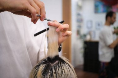 Kuaför, genç bayan müşterinin saç uçlarını makas ve tarakla kesiyor.