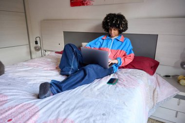 Dizüstü bilgisayarı üzerinde çalışan ve rahat bir yatak odasında rahat bir şekilde dinlenen kız öğrenci sıradan bir çalışma yaşam tarzını benimsiyor.