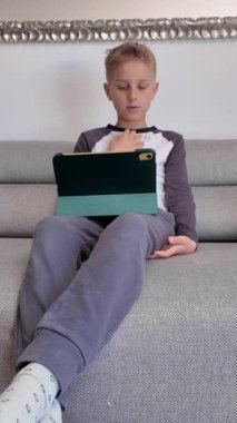 Dijital aktivitesine kendini kaptırmış, koltukta otururken tablet kullanan bir çocuğun görüntüsü.