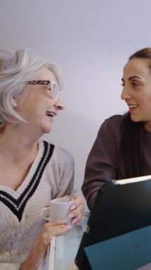 Yaşlı kadın ve kız bir tablete bakıp gülerken bir anlık neşe paylaşıyorlar.