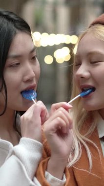 Genç bayan çift kalp şeklindeki lolipoplarını paylaşıyor, romantik yakınlık ve duygusal yakınlığı yumuşak ağır çekimde neşeli bir hareketle ifade ediyorlar.