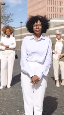 Şehir ortamında poz veren kendine güvenen iş kadını, arka planda duran meslektaşlar, yavaş çekim etkisi