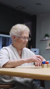 Kıdemli kadın bilişsel egzersizler yapıyor, renkli oyuncakları yavaş çekimde masada manipüle ediyor.