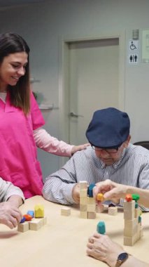Kıdemli adam renkli blokları olan bir binada canlandırıcı bir aktiviteye girişiyor. Sağlık hizmetlerinde çalışan destekleyici bir hemşire tarafından destekleniyor.