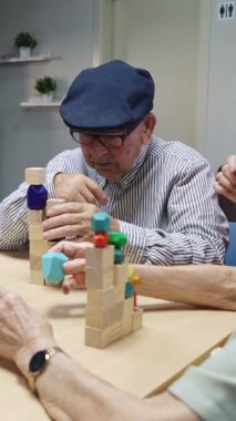 Kıdemli adam renkli tahta blokları hemşirelerden yardım alarak diziyor, motor becerilerini ve bilişsel fonksiyonlarını yavaş çekimde geliştiriyor.