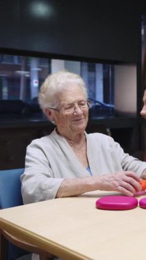Son sınıf öğrencisi kadın renkli disklerle oynamayı seviyor, onları bir huzurevinde yavaş çekimde masaya dizmeyi seviyor.