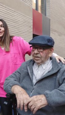 Şefkatli hemşire, dışardaki bağlantı ve sağlık anlarında tekerlekli sandalyedeki yaşlı adama nazikçe rehberlik ediyor.