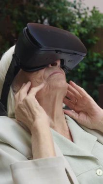 VR kulaklık takan yaşlı kadın sanal gerçekliği tecrübe ediyor, yüzüne dokunuyor ve ellerini yavaş çekimde hareket ettiriyor.