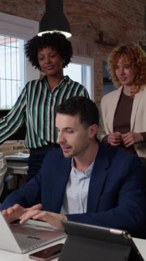 İşbirliği bürosu toplantısında dizüstü bilgisayarda yazan profesyonel işadamı, işyeri dinamiklerini yavaş çekimde izleyen kadın meslektaşlar