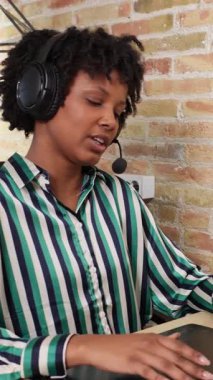 Kulaklıklı genç siyahi kadın tele pazarlamacı olarak çalışıyor ve yavaş çekimde müşteriyle konuşuyor.