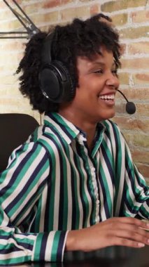 Bilgisayar başında çalışırken kulaklık takan ve gülümseyen dost canlısı müşteri hizmetleri temsilcisi.