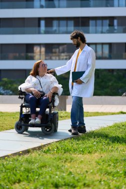 Parkta tekerlekli sandalyeli engelli bir kadını destekleyen doktor.