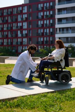 Şehir parkında tekerlekli sandalyede engelli hastaya yardım eden doktor.