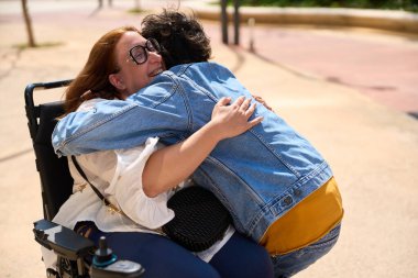 İki arkadaş neşeyle kucaklaşıyorlar açık havada, samimi bir anda.