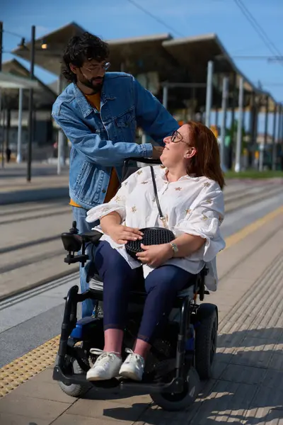 Adam, toplu taşıma istasyonunda tekerlekli sandalye kullanan bir kadını destekliyor, dahil olma ve erişilebilirliği teşvik ediyor.