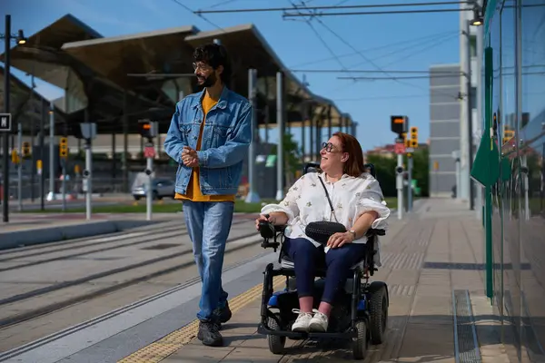 Adam, tramvay durağına yaklaşan bir kadının yanında yürür. Toplu taşımacılıkta ulaşılabilirlik ve kapsayıcılığı gösterir.