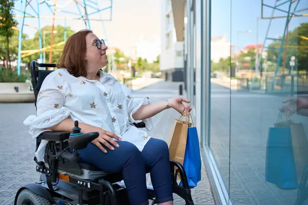 Engelli bir kadın alışveriş çantalarını taşırken şehrin penceresinden geçerken gülümsüyor.