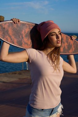 İskelede uzun tahta tutan şık bir kadın gözlerini kaçırıyor, kumsalda altın saat günbatımının tadını çıkarıyor.