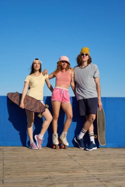 Üç şık arkadaş güneşli bir günün tadını çıkarıyor. Kaykay ve paten tutkusu sergiliyorlar.