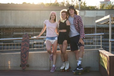 Üç havalı arkadaş kaykay parkında takılıyor, şehir sporlarının ve altın güneş ışığında gençlik yaşam tarzının tadını çıkarıyorlar.