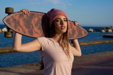 Arka planda deniz olan bir plajda uzun tahta tutan genç bir kadın yaz günbatımının tadını çıkarıyor.