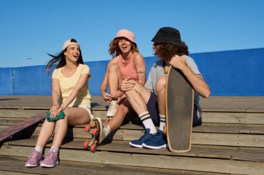 Bir grup genç yaz kıyafeti giyiyor, oturuyor ve parkta eğleniyor, konuşuyor ve birlikte gülüyor.