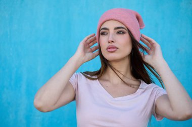 Pembe bereyi ayarlayan zarif genç bir kadın canlı mavi duvara karşı poz verirken modaya uygun moda ve kentsel tarzı sergiliyor.