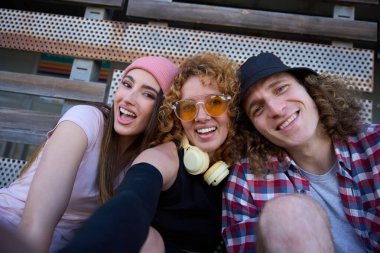 Üç genç, şık arkadaş dışarıda birlikte oturuyorlar, mutlu bir şekilde gülüyorlar.