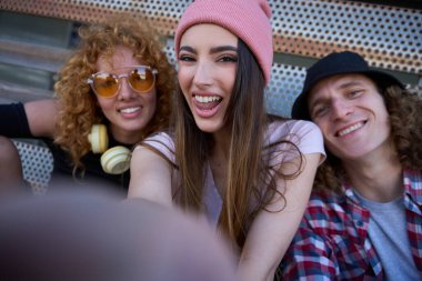Dışarıda güneşli bir günün tadını çıkaran üç neşeli genç arkadaş eğlenceli bir selfie ve mutluluk saçan mutlu anları yakalıyorlar.