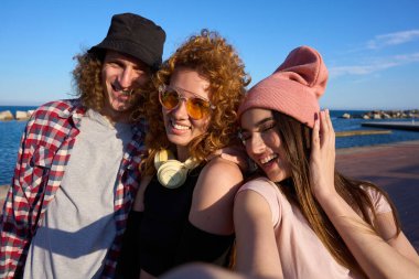 Üç genç arkadaş deniz kenarında neşeli bir selfie çekiyorlar, güneşleniyorlar ve güzel bir günde arkadaşlıklarını kutluyorlar.