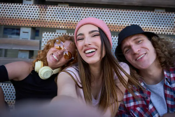 Üç neşeli arkadaş birlikte eğlenceli bir anı yakalıyorlar, gençlik enerjilerini ve bağlantılarını şehir ortamında ifade ediyorlar.