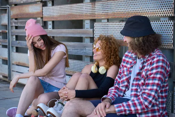 Üç neşeli genç arkadaş yerde birlikte oturuyorlar, birbirlerine eşlik ediyorlar ve kahkahalarını paylaşıyorlar.