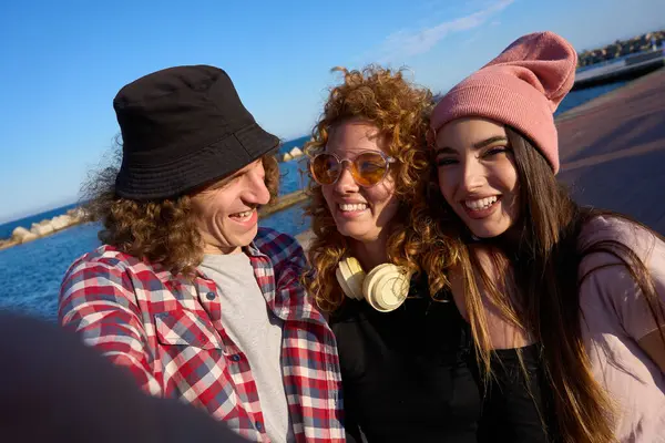 Güneşli bir günde deniz kenarında selfie çeken üç neşeli arkadaş birlikte vakit geçiriyorlar.