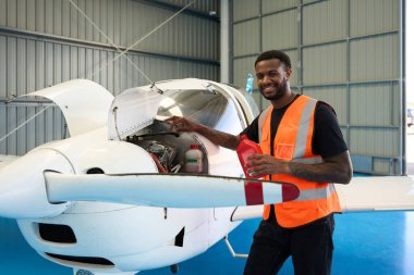 Gülümseyen uçak teknisyeni bir havacılık hangarında küçük bir uçak motorunun bakımını yaparken elinde bir şişe yağ tutuyor.