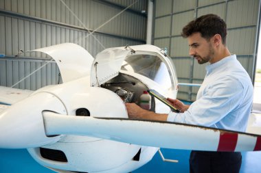Uçak tamircisi, havacılık hangarında küçük bir uçağın motorunu incelerken dijital tablet kullanır.