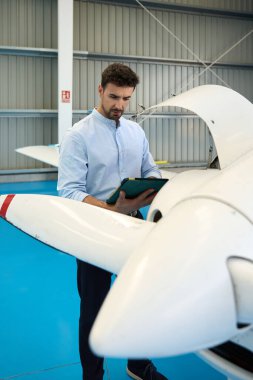 Bir hangarda küçük bir uçak motorunu incelerken dijital tablet kullanan uçak teknisyeni, bakım ve güvenliği garanti altına alıyor.