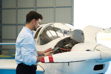 Uçak tamircisi, hangardaki küçük bir uçağın motorunda bakım kontrolü yapmak için dijital tablet kullanır.