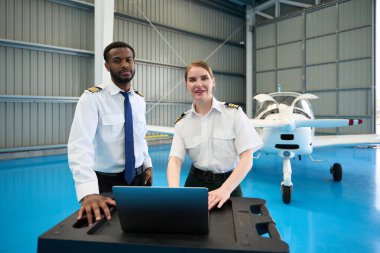 İki öğrenci pilot havacılık eğitimi için küçük bir uçakla bir hangarda dizüstü bilgisayar kullanıyor.