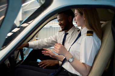 İki öğrenci pilot, bir erkek ve bir kadın, küçük bir uçağın kokpitinde oturuyorlar ve kontrolleri öğreniyorlar.