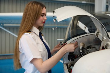 Hangarda uçak motorunda çalışan genç kadın uçak tamircisi bakım ve onarım işleri yapıyor.