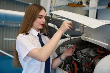 Kendine güvenen kadın uçak teknisyeni bir hangarda uçuş öncesi denetim sırasında küçük bir uçak motorunun yağ seviyesini kontrol ediyor.