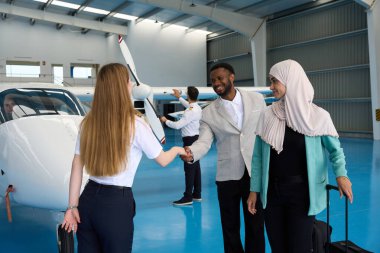 Kadın pilot, yolcuları bir uçak hangarında sıcak bir tokalaşmayla karşılıyor ve özel uçuşlarından önce hoş bir atmosfer yaratıyor.