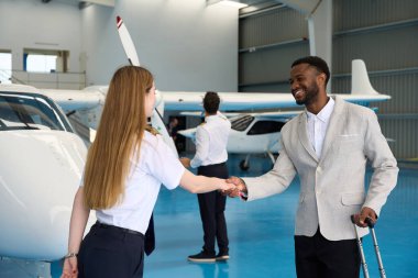 Kadın pilot, uçak hangarında bir işadamıyla el sıkışıyor, anlaşma yapıyor.