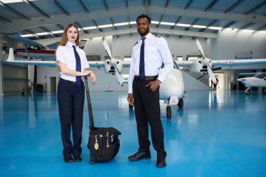 Bir hangarda, uçuş çantası ve uçaklarla güvenle duran iki öğrenci pilot havacılık eğitimi için hazır.