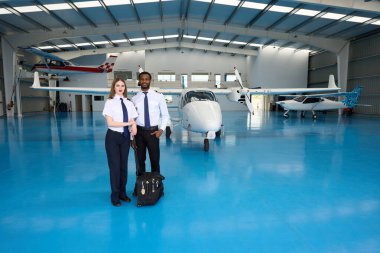 Bir hangarda elinde hafif uçaklarla bekleyen iki pilot öğrenci bir sonraki antrenman için hazırlar.